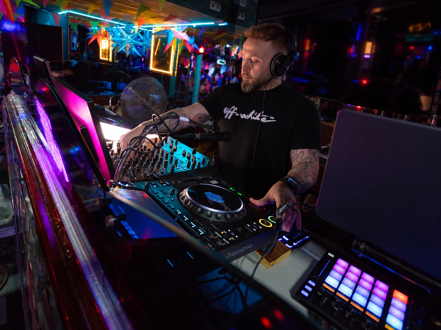 Ash Jenkins performing at a nightclub DJ booth in a black T-shirt