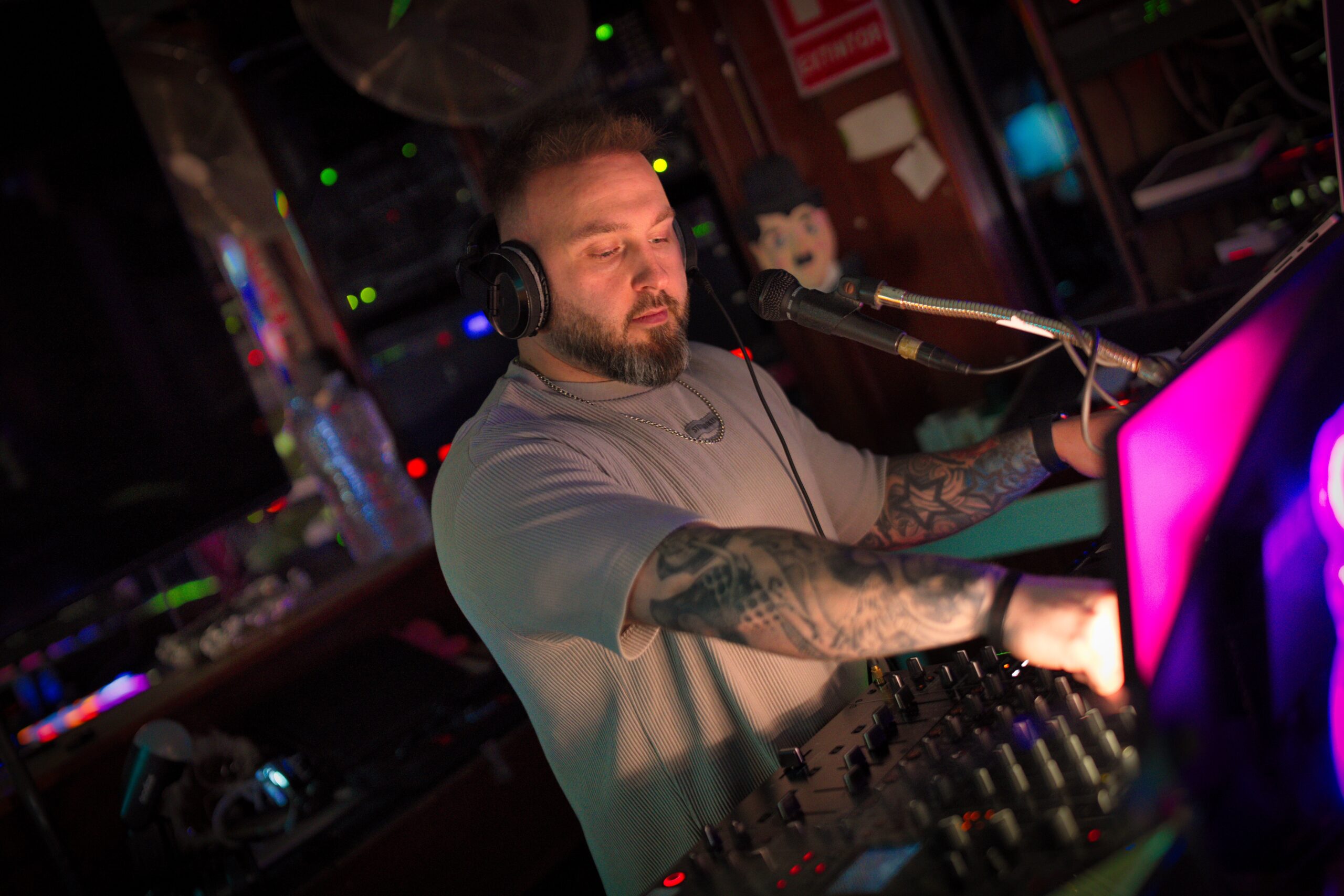Ash Jenkins performing at a nightclub DJ booth in a grey T-shirt
